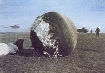 Gagarin's alleged landing capsule on
                              a meadow with recovery by helicopters in
                              the background. The abrasion is different
                              to the landing capsules before.