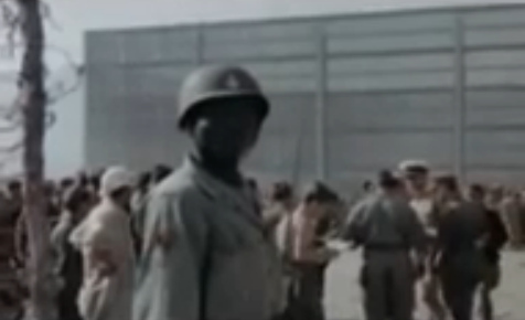 Black "U.S." army member
                          standing before a wooden wall