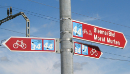 Corcelles: Route des Grands Longs Champs,
                          Wegweiser am Bahnübergang für Velorouten